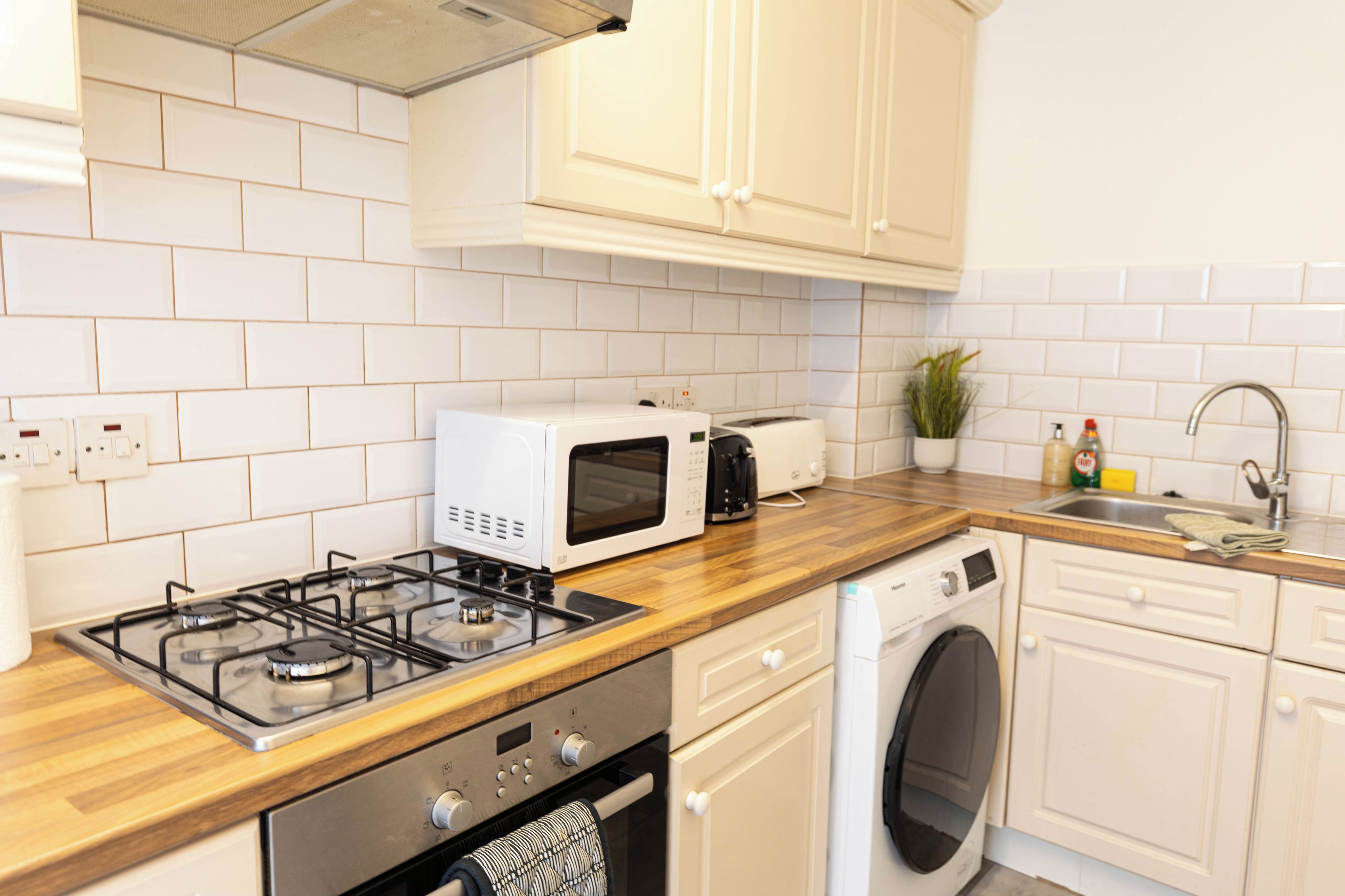 Een moderne keuken met witte kasten, een gasfornuis, een magnetron, een broodrooster en een ingebouwde wasmachine.