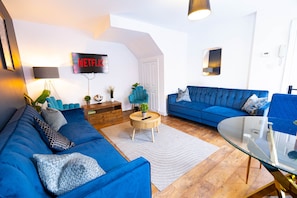 A modern living room with a blue sofa set, a wooden coffee table, and a flat-screen TV mounted on the wall. - 2/3 BR Duplex House | Sleeps 6 | 2-minute walk from Camden Town Tube Station (London)