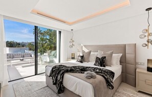 Ein modernes Schlafzimmer mit einem großen Bett, einer Glastür, die auf einen Balkon führt, und Blick auf die Stadt.