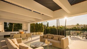 A modern outdoor living space with a sofa, chairs, a dining table, and a grill. - Vrbo Property (Nueva Andalucía)