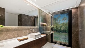 A modern bathroom with a large mirror, a white sink, and a glass shower enclosure. - Vrbo Property (Nueva Andalucía)