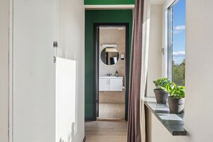 Un pasillo que conduce a un baño con espejo, lavamanos y plantas en macetas.