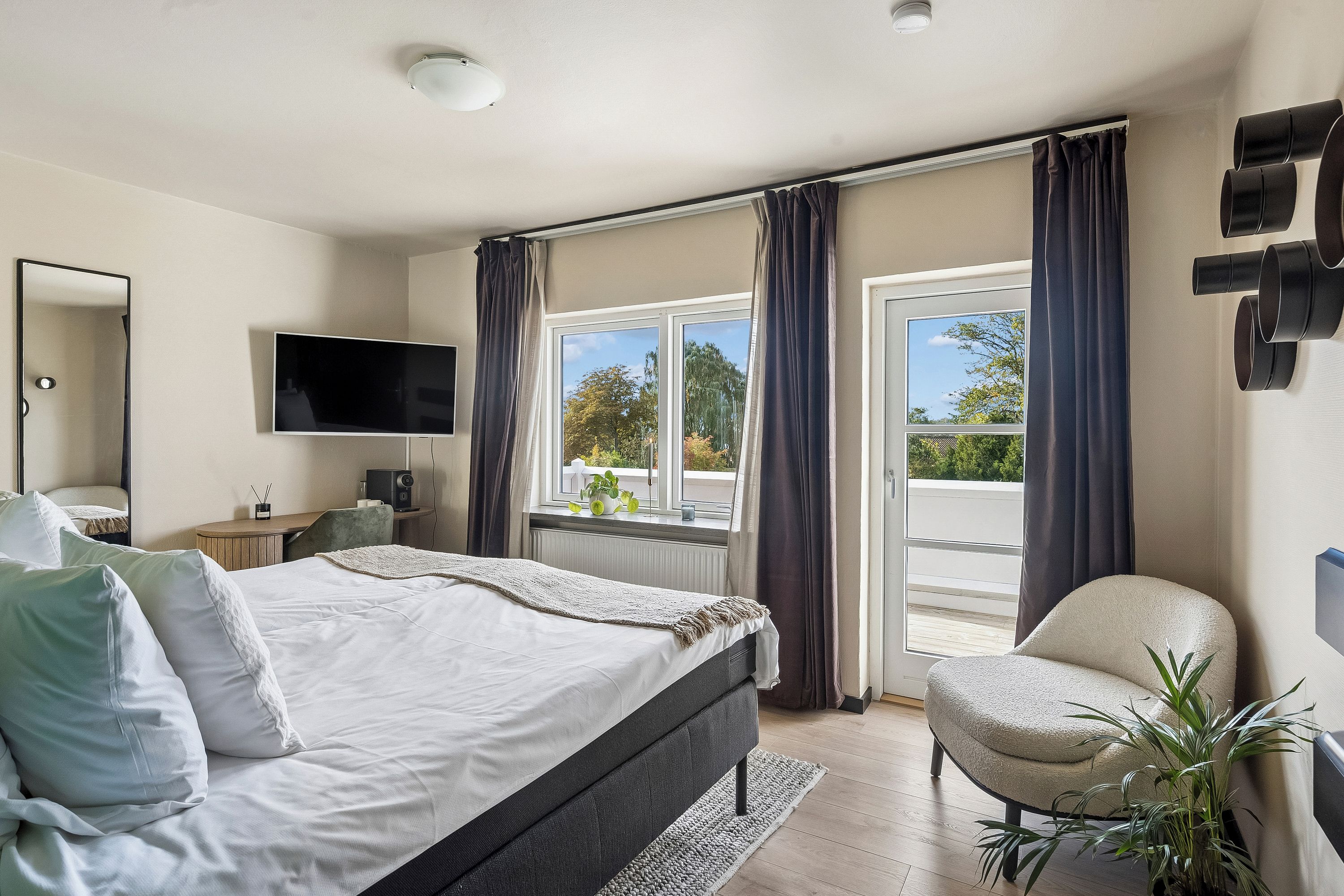 Ein Schlafzimmer mit einem Bett, einem Sessel, einem Fernseher und einem Fenster mit Vorhängen.