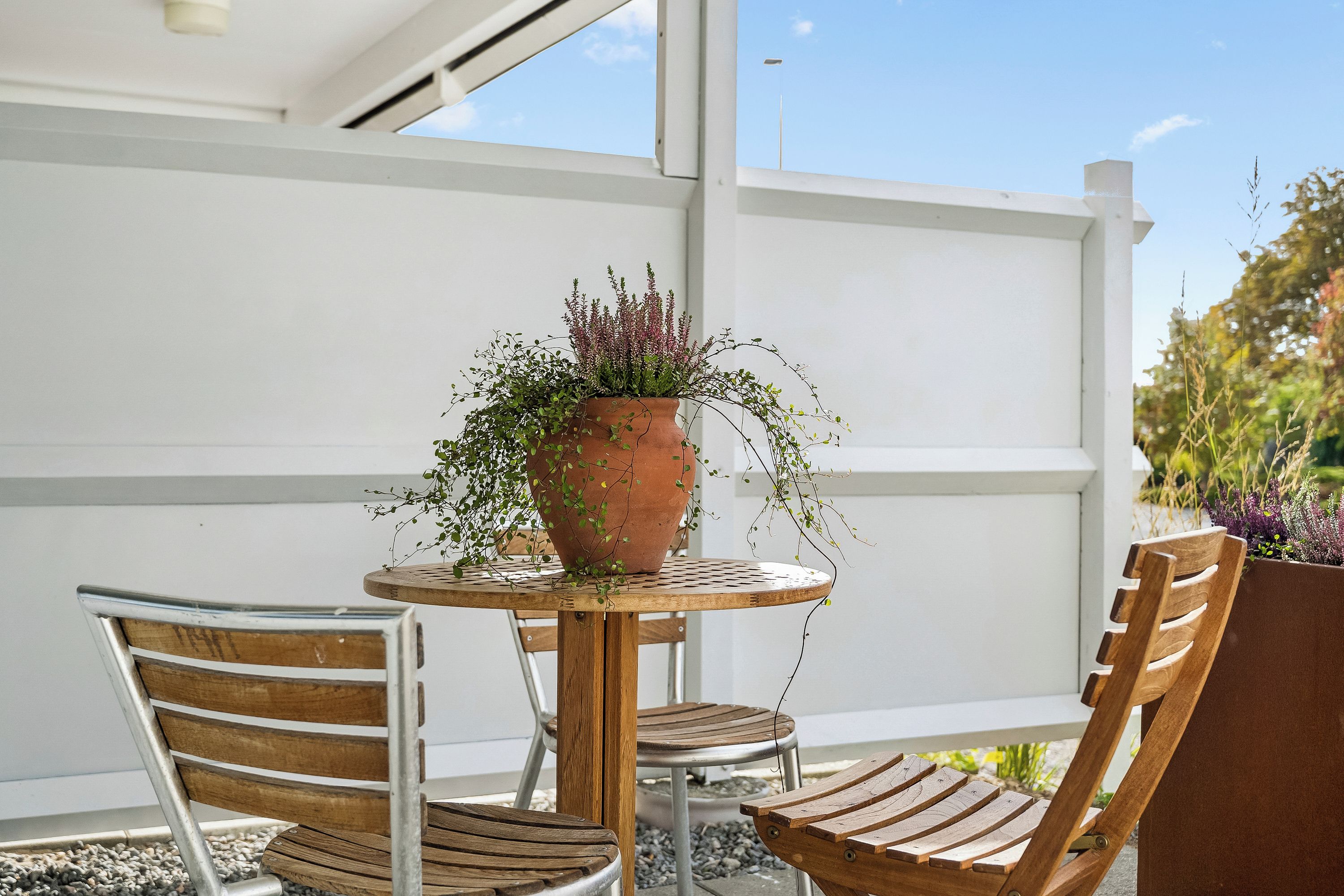 A round table with a terracotta pot on top, two wooden chairs, and a white wall in the background.