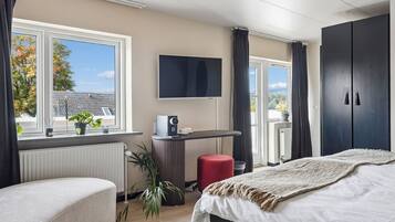 A modern bedroom with a bed, a desk, a TV, and a view of the outdoors.