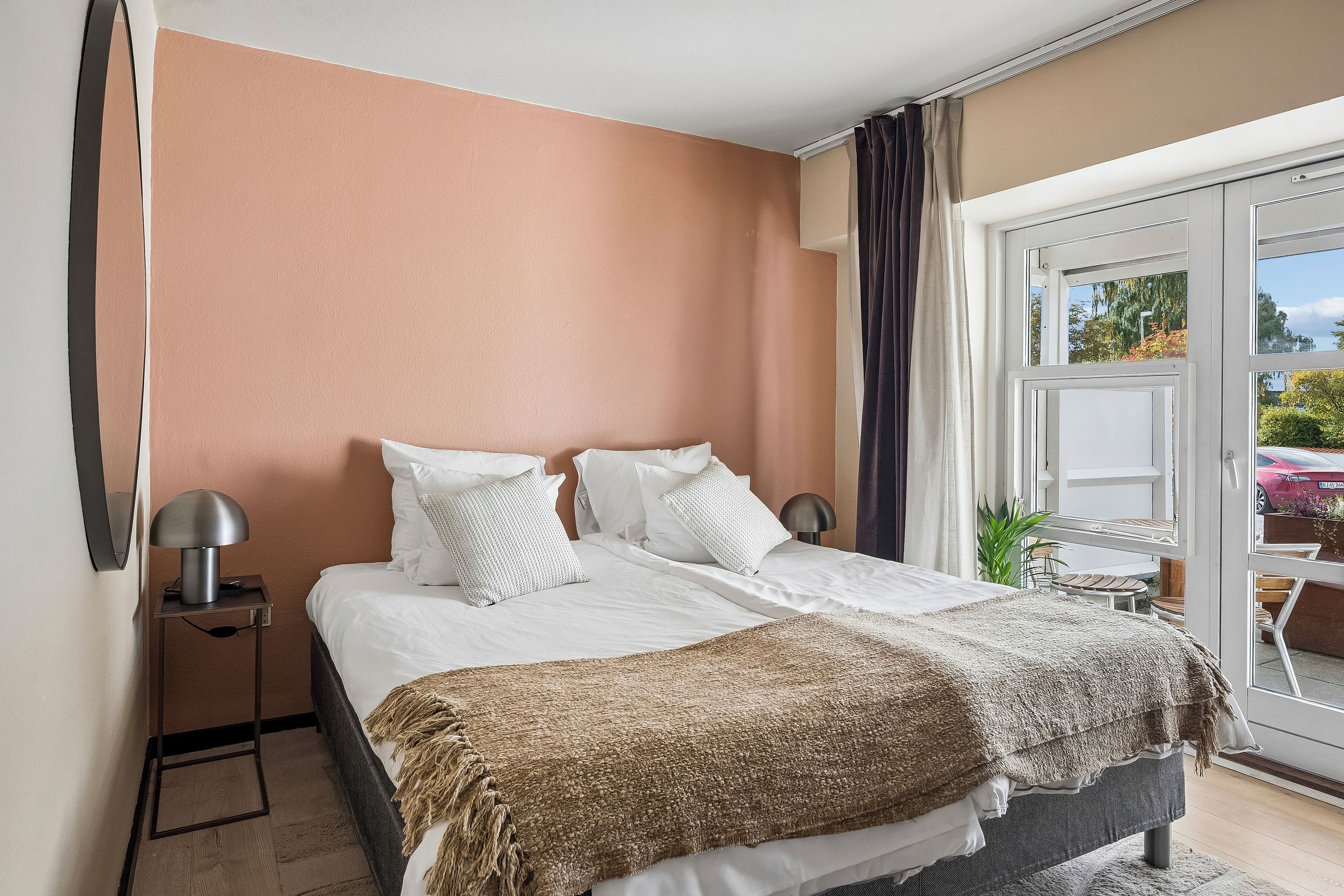 A hotel room with a bed, bedside tables, a window with curtains, and a view of the outdoors.