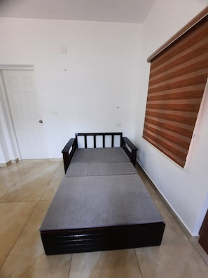 A room with a bed, a door, and a window with blinds. - THESSALIA (Aluva)