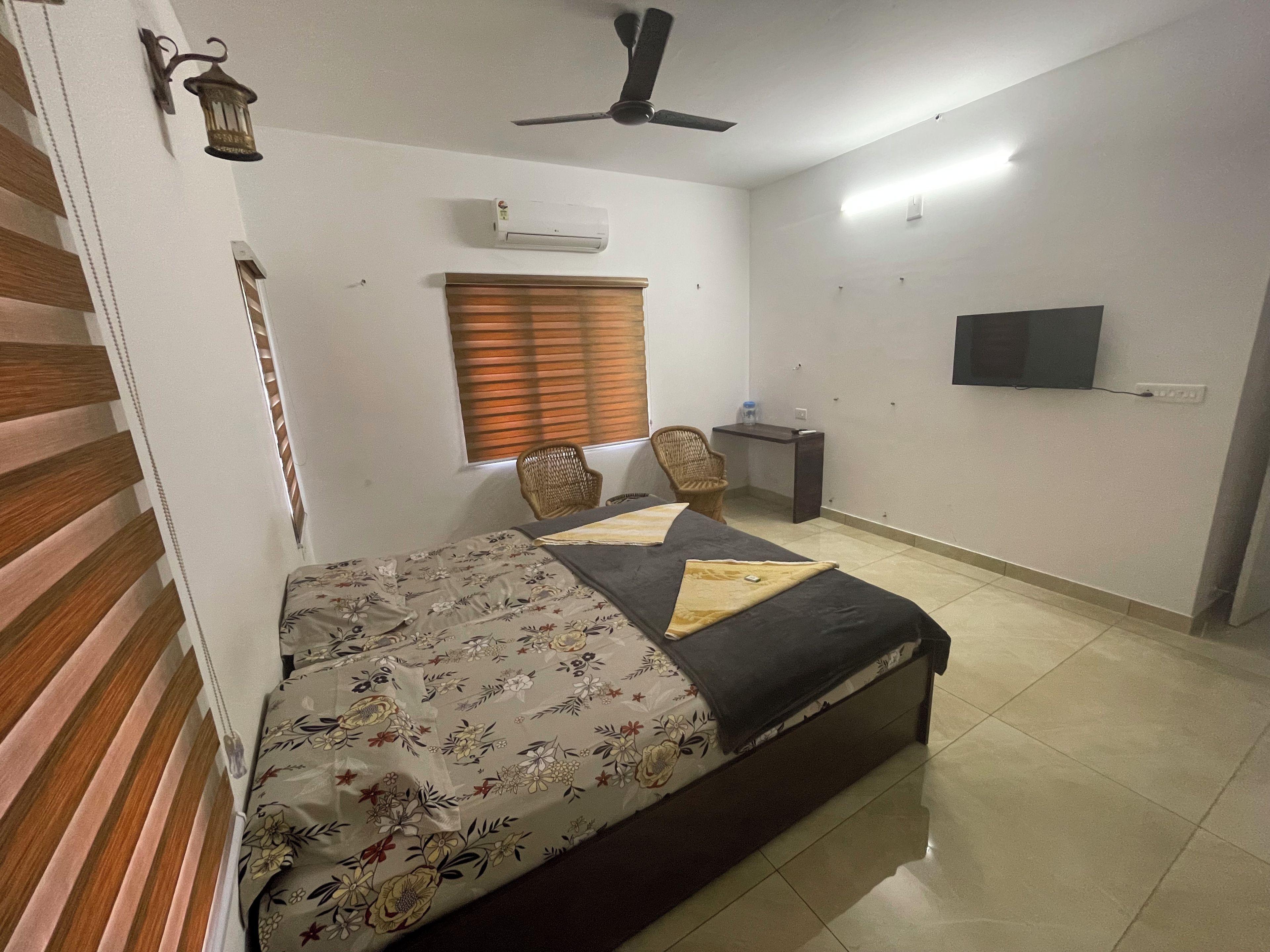 A bedroom with a bed, a desk, a chair, a ceiling fan, and a TV on the wall.