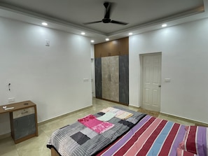 Un dormitorio con cama, escritorio, armario y ventilador de techo.