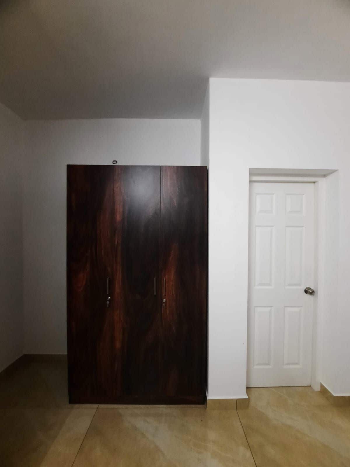 Una habitación con un armario de madera oscura, una puerta blanca y suelo de baldosas.