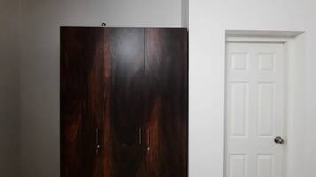 Una habitación con un armario de madera oscura, una puerta blanca y suelo de baldosas.