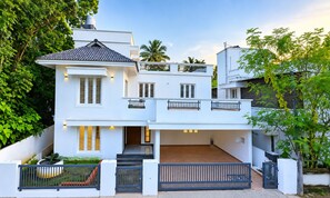 A two-story house with a balcony, a covered patio, and a gated entrance. - THESSALIA (Aluva)