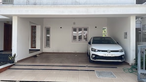 A white car parked in a covered parking area with tiled flooring and a white wall. - THESSALIA (Aluva)