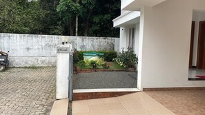 A gated entrance to a property with a paved driveway, a concrete wall, and a small garden area with a water feature.