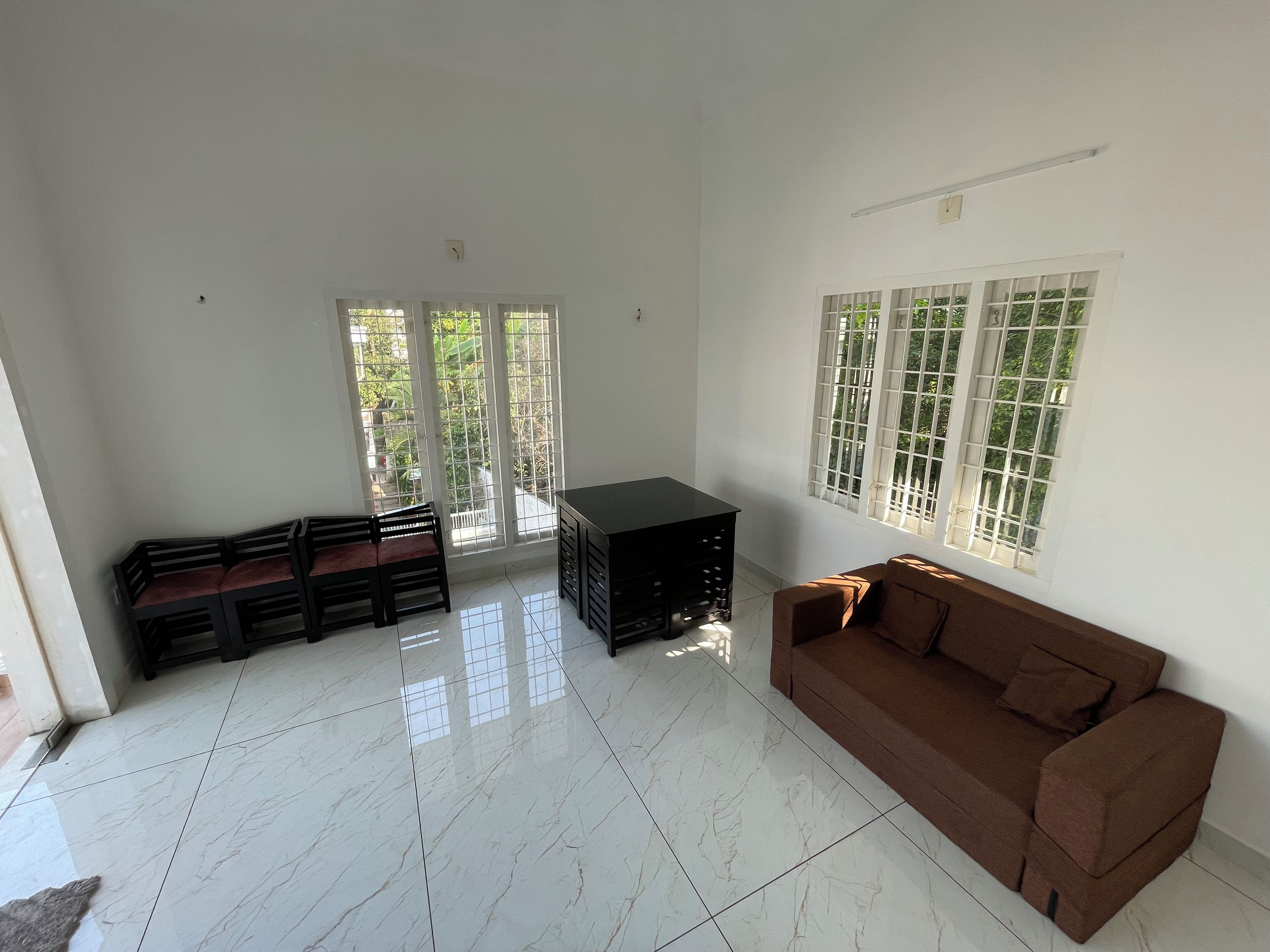 Una habitación con un sofá marrón, un mueble negro y suelo de baldosas.