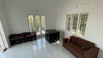 Una habitación con un sofá marrón, un mueble negro y suelo de baldosas.