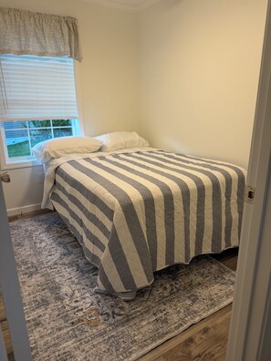 Ein Schlafzimmer mit einem Bett, einem Fenster mit Jalousien, einem gemusterten Teppich und einer Tür.
