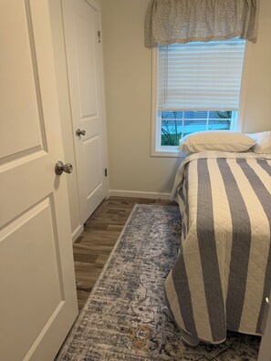 Ein Schlafzimmer mit einem Bett, einem Fenster mit Jalousien, einer Tür und einem gemusterten Teppich.