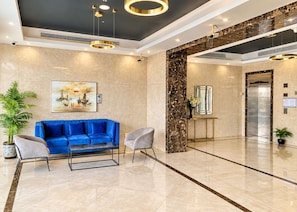 Eine moderne Lobby mit einem blauen Sofa, einem Couchtisch, einer Topfpflanze, einem Gemälde und einem Aufzug.