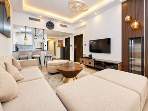 Ein modernes Wohnzimmer mit einer Eckcouch, einem Couchtisch, einem Fernseher und einer Küche im Hintergrund.