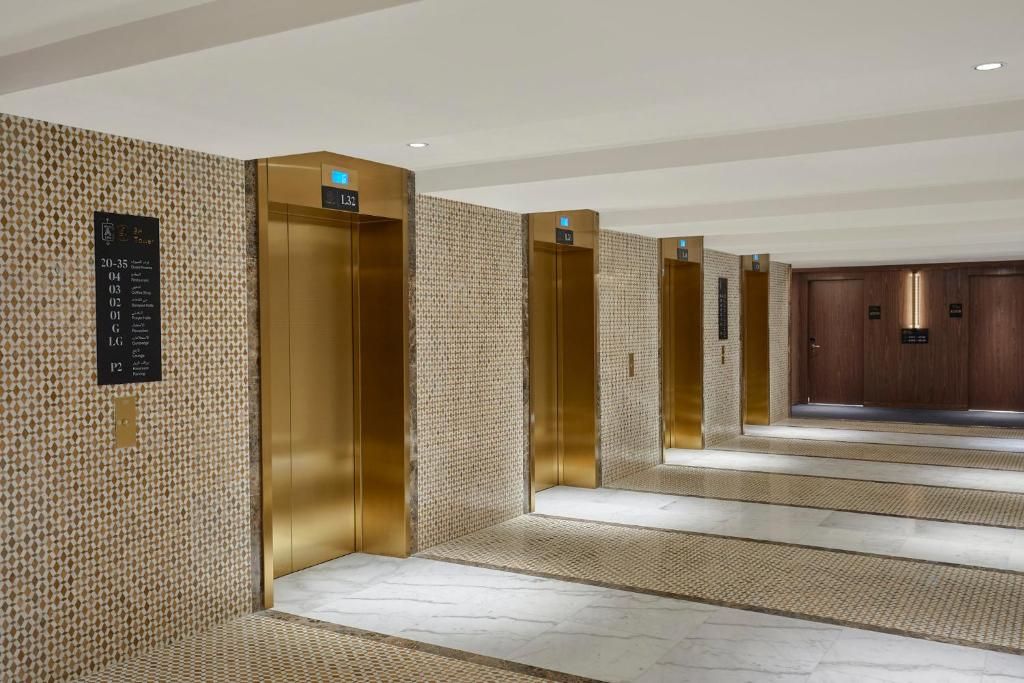 A hotel lobby with a patterned wall, a reception desk, and a series of elevators.