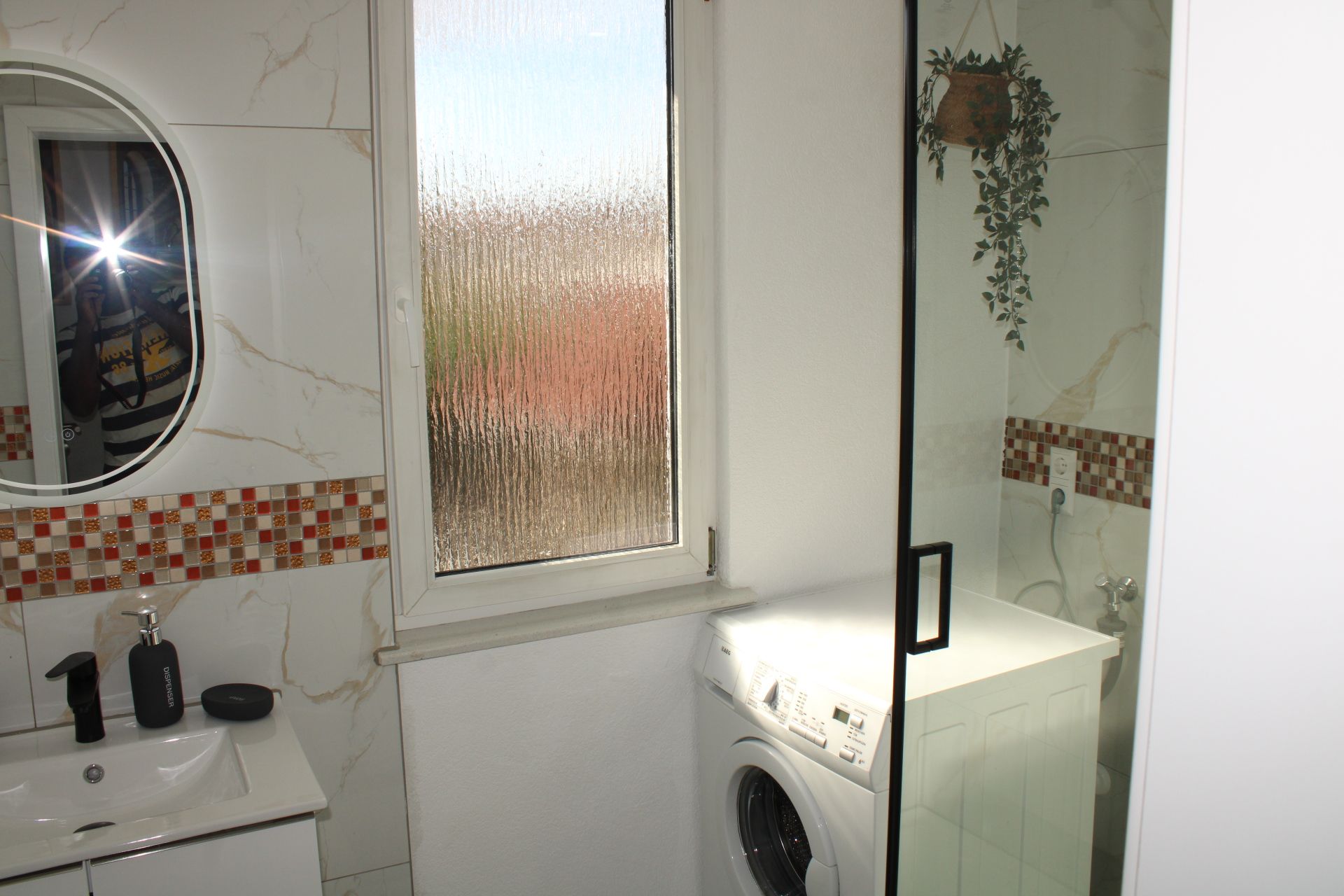 Ein Badezimmer mit Waschmaschine, Waschbecken mit Spiegel und Duschbereich.