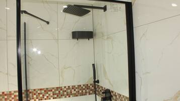 Eine gläserne Dusche mit schwarzem Rahmen, einer Handbrause und einer an der Wand befestigten Bedienfeld.