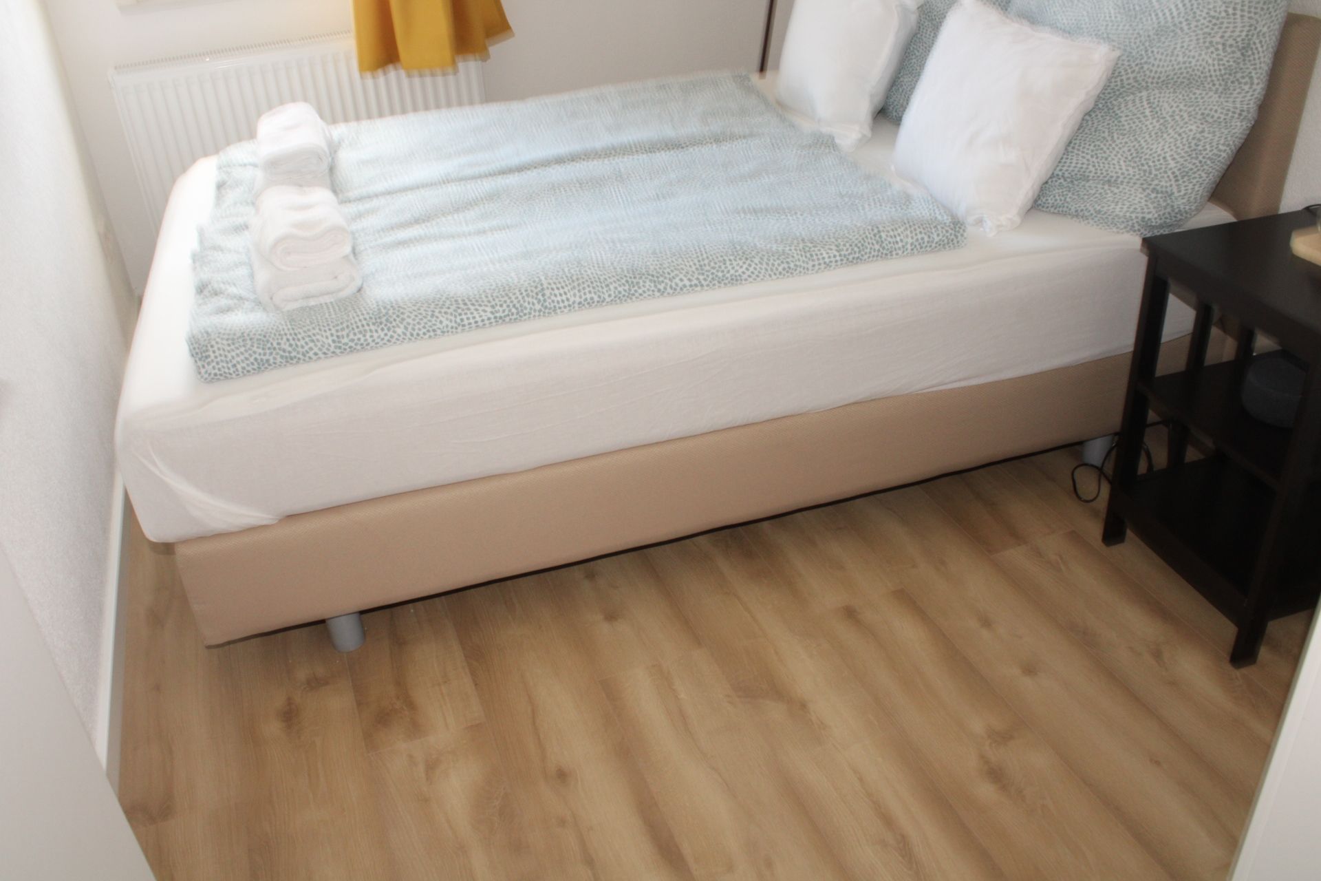 Un lit simple avec un matelas blanc et une couverture bleu clair, placé contre un plancher en bois.