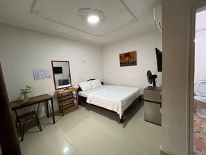 A bedroom with a bed, a desk, a chair, a small table, a fan, and a refrigerator. - Naraya Guesthouse (Phnom Penh)