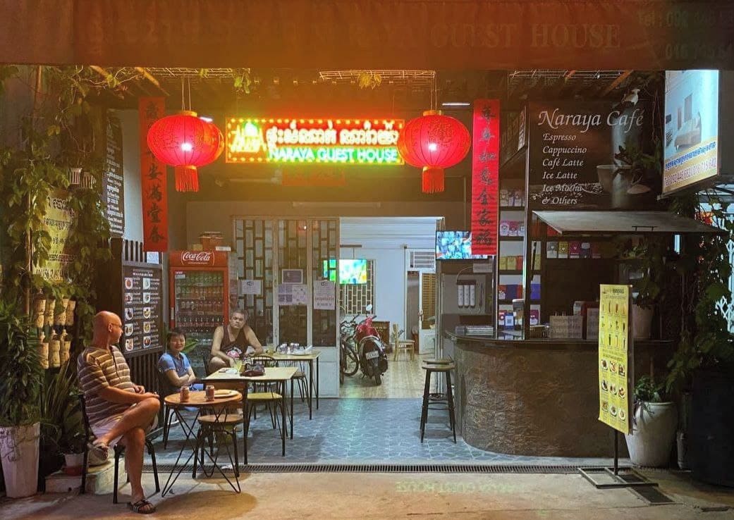 A café interior with tables and chairs, a counter, and a neon sign above the entrance.