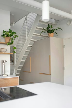 A modern kitchen with a white countertop, a built-in stove, and a staircase with a white railing. - Two-storey flat with private garden (København S)