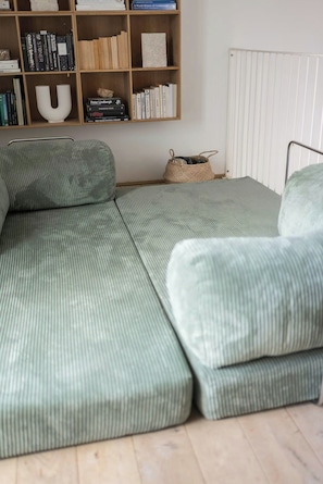 A green sofa with a woven basket and a bookshelf with books and decorative items. - Two-storey flat with private garden (København S)