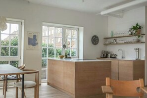 A modern kitchen with a central island, wooden cabinetry, and a dining area with chairs. - Two-storey flat with private garden (København S)