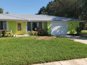 Einbungalow mit Garage, Eingangstür und kleinem Vorgarten mit Rasen und Pflanzen.