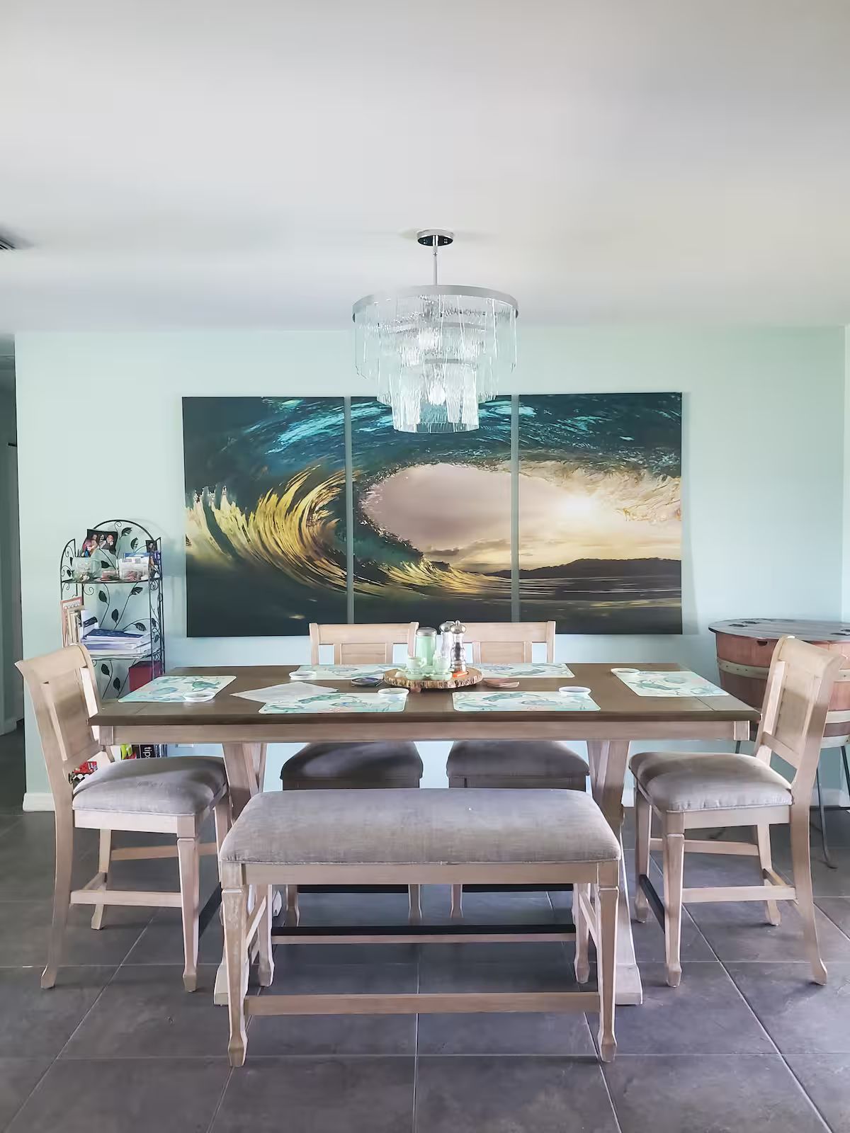 A dining area with a large painting, a chandelier, and a wooden table set for four.