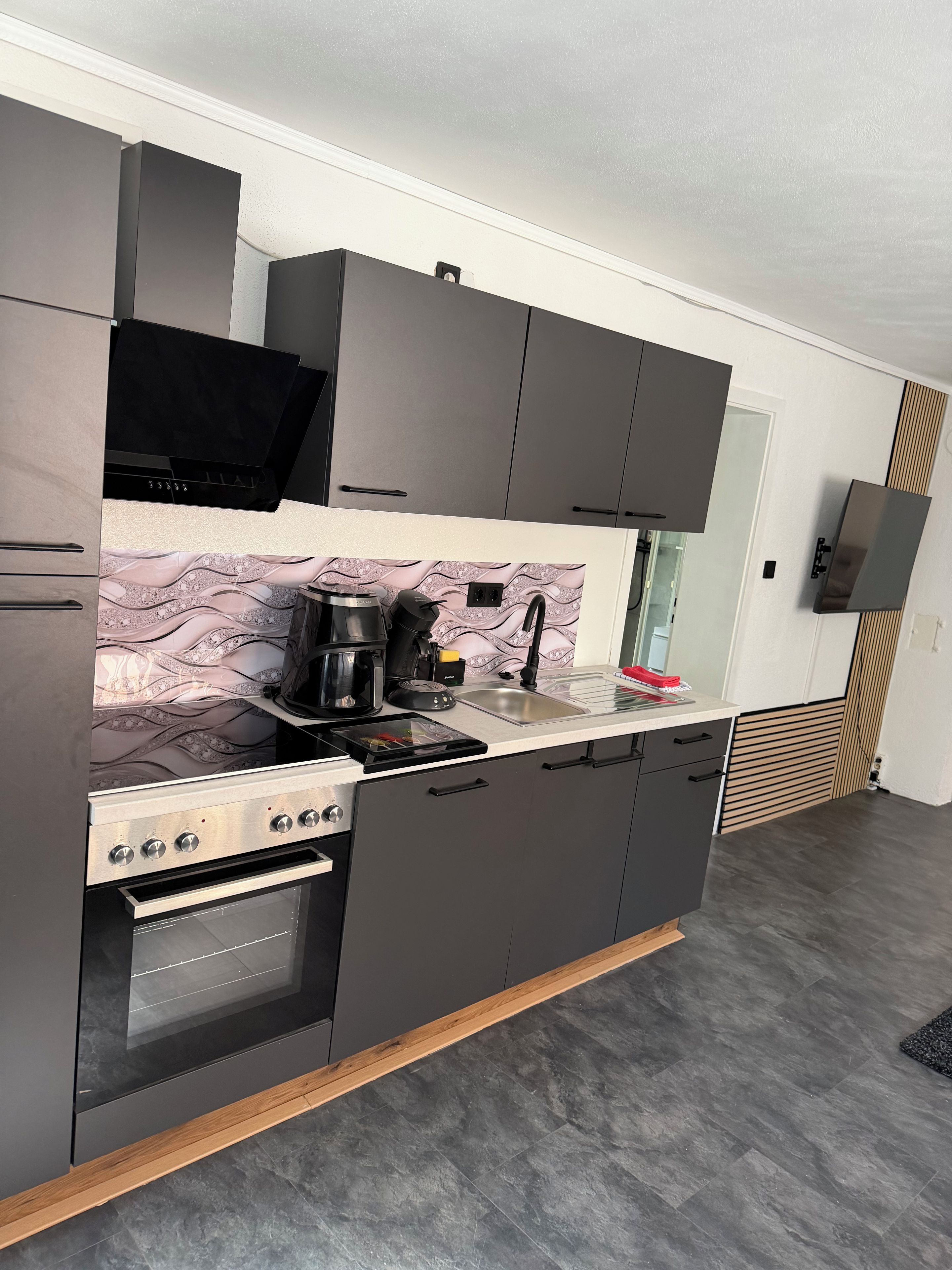 A modern kitchen with dark cabinetry, a built-in oven, and a countertop with a coffee maker and other appliances.