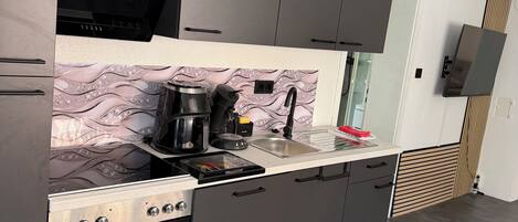 A modern kitchen with dark cabinetry, a built-in oven, and a countertop with a coffee maker and other appliances.