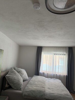 Ein Schlafzimmer mit einem Bett, Kissen, einem Fenster mit Vorhängen und einer Deckenleuchte.