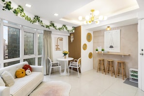 A modern living room with a sofa, chairs, a dining table, and a kitchen area with stools. - Spacious 2BR BGC Stay City View Fort Victoria Family & Group Friendly (Taguig)