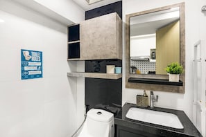 A modern bathroom with a toilet, sink, and mirror. There is a blue sign with toilet rules on the wall. - Spacious 2BR BGC Stay City View Fort Victoria Family & Group Friendly (Taguig)