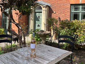 A wooden table with wine glasses and a bottle, set outdoors with a brick building and greenery in the background. - Kylemore (Glastonbury)