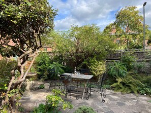 An outdoor patio with a table and chairs, surrounded by lush greenery and a stone wall. - Kylemore (Glastonbury)