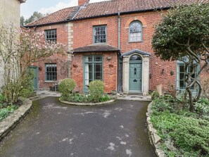 A traditional brick house with a central entrance, a small garden with a circular flower bed, and a paved driveway. - Kylemore (Glastonbury)