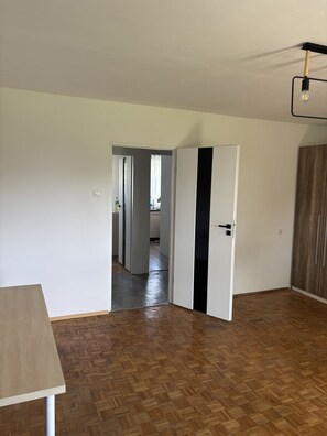 A room with a wooden floor, a white door, and a hallway leading to another room. - Urokliwe Apartamenty (Konin)