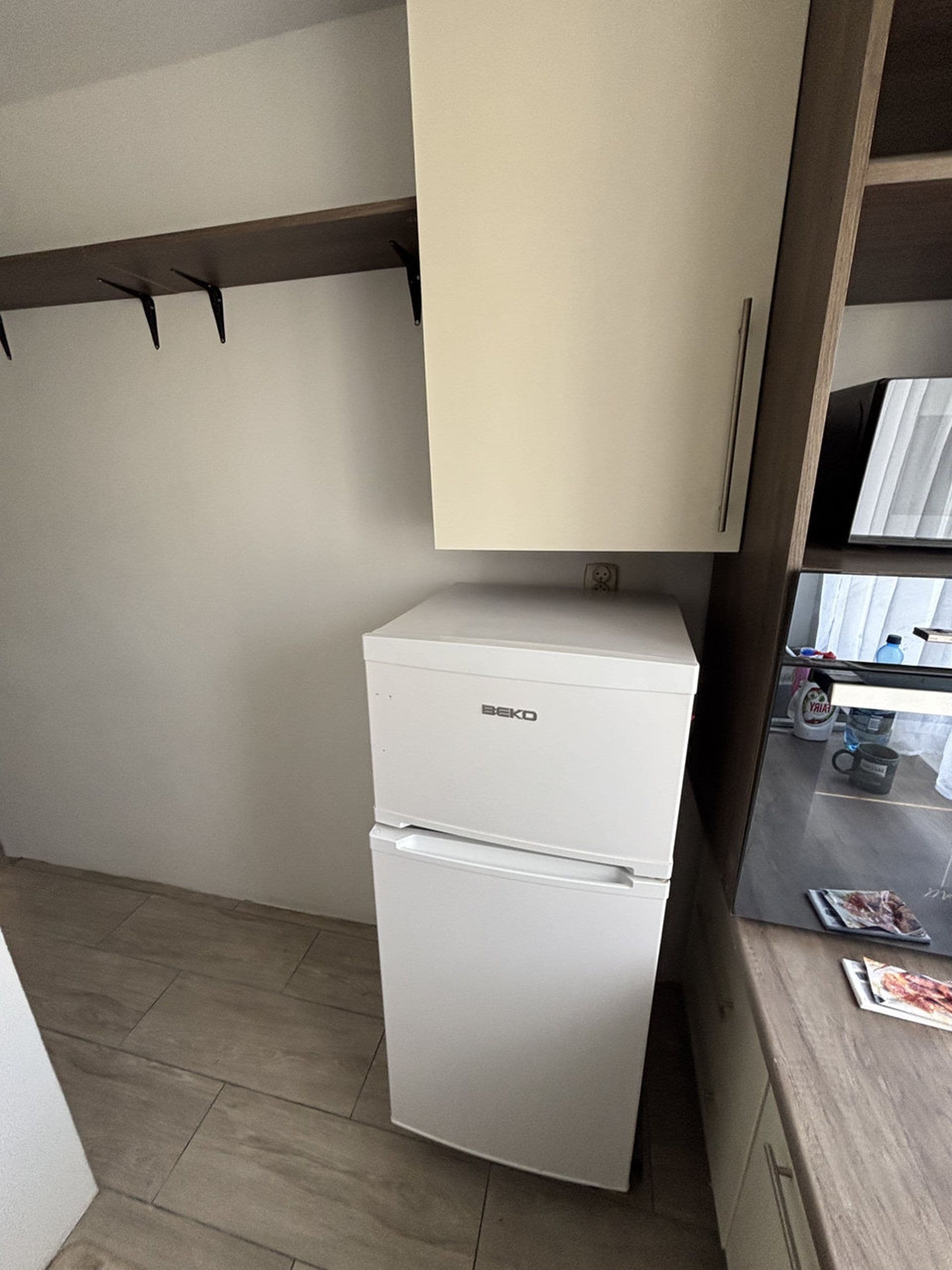 Una kitchenette compacta con un refrigerador blanco, un estante de madera y una encimera con una botella de agua y una taza.