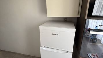 Una kitchenette compacta con un refrigerador blanco, un estante de madera y una encimera con una botella de agua y una taza.