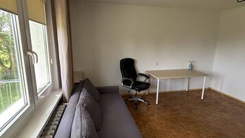 A room with a grey sofa, a black office chair, a wooden floor, and a window with curtains.