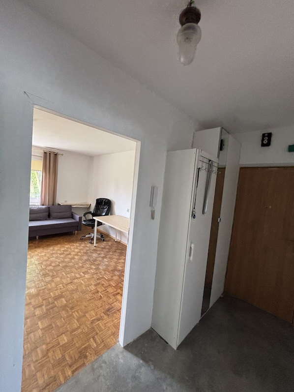 A room with a wooden floor, a white wardrobe, a bench, a sofa, and a ceiling light fixture.