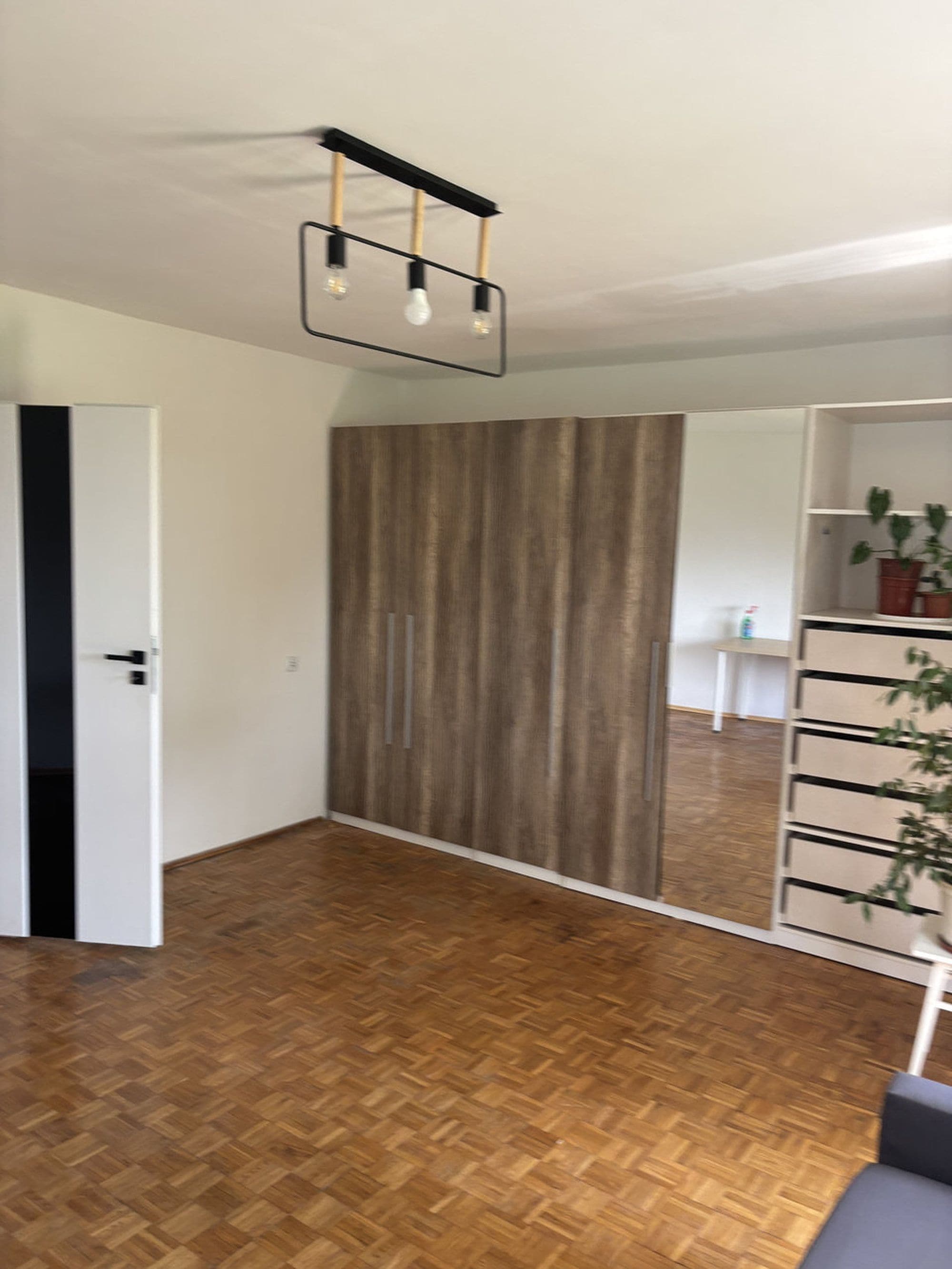 A room with a herringbone wooden floor, a wardrobe with a vertical striped pattern, and a ceiling light fixture.