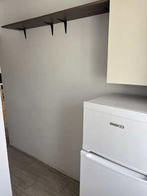 A kitchen with a white refrigerator, a wooden shelf, and a white cabinet.